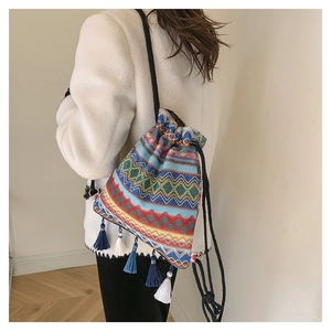Borsa a secchiello etnica intrecciata con motivi geometrici colorati e nappe su modella