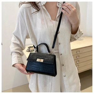 Fashionable black crocodile pattern handbag with gold hardware worn by a model