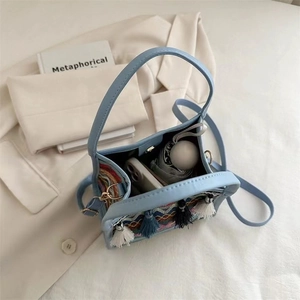 Borsa a mano azzurra in ecopelle con ricami colorati e nappe su sfondo di abito bianco
