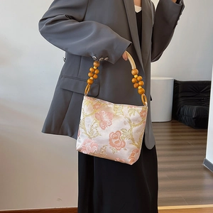 Elegant tote bag with pink gold floral embroidery and wooden bead handles on grey blazer