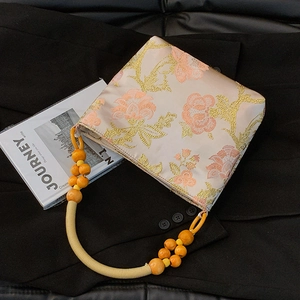 Pink satin tote bag with floral embroidery and wooden bead handles on a dark background