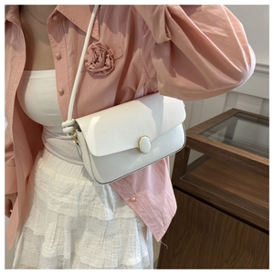 Détail du sac à bandoulière blanc minimaliste avec boucle dorée et nœud sur le côté