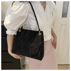 Detail of black tote bag with ruched texture, gold eyelets and embossed fashion text