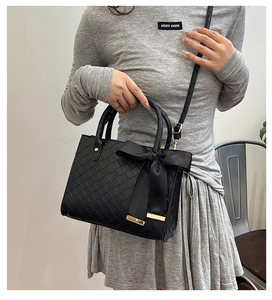 Détail du sac cabas en cuir tressé noir avec un grand nœud en satin et accents dorés