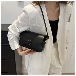 Sac bandoulière noir avec boucle dorée porté sur un ensemble de costume blanc