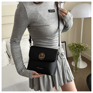 Détail d'un sac bandoulière en cuir noir avec emblème doré porté par le mannequin