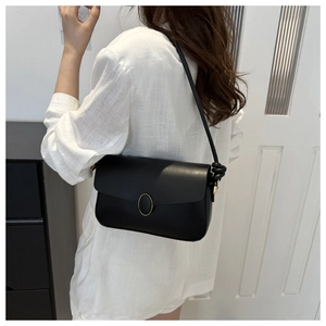 Sac à bandoulière minimaliste en cuir noir mat avec boucle dorée sur chemise blanche