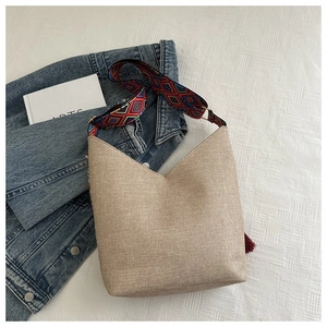Detail van canvas tas met bohemien schouderband en donkerrode kwastjes hanger