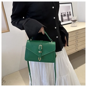 Detail of green leather handbag with gold belt buckle clasp and envelope flap design