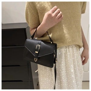 Detail of a chic black leather crossbody bag featuring a golden U-shaped buckle decoration