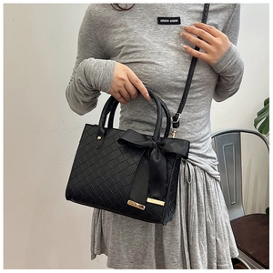 Détail d'un sac cabas noir tissé avec un nœud en soie et une garniture en métal doré