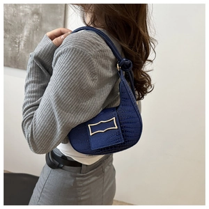 Detail of dark blue faux crocodile leather baguette bag with golden buckle and knot strap