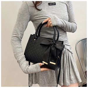 Détail du sac cabas tressé noir avec un grand nœud en satin et finitions dorées