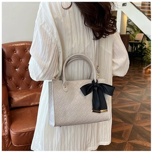 Sac fourre-tout gris tressé avec nœud noir porté par un mannequin en robe blanche chic
