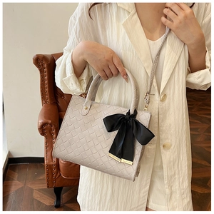 Gros plan du sac cabas beige tressé avec nœud noir et détails métalliques dorés