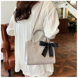Détail du sac cabas tressé gris clair avec un grand nœud en satin noir élégant
