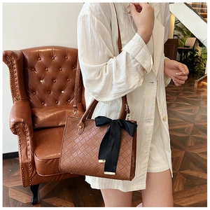Grand sac cabas marron tissé avec nœud noir porté par un mannequin dans un salon