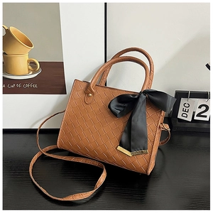 Détail du sac cabas tressé marron avec grand nœud en satin noir et bord doré