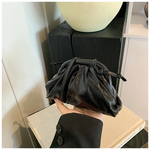 Detail of a black glossy pleated dumpling bag with leather texture and soft knotted strap