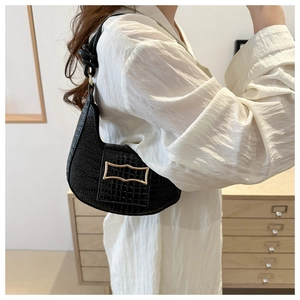 Detail of a black faux crocodile baguette bag with a gold buckle worn on the shoulder