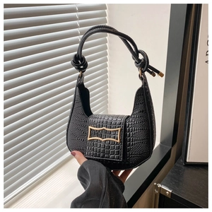 Macro detail of black crocodile embossed faux leather handbag with golden buckle and knot handle
