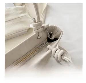 Close-up of cream textured tote bag featuring a smooth metal zipper and leather knot detail