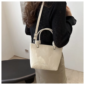Close-up of cream leather bucket bag featuring woven rope handle and silver hardware