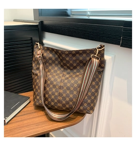 Detail of a brown geometric tote bag with striped woven strap on a wooden desk