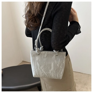 Minimalist light grey pleated bucket bag with long strap shown on model outdoors