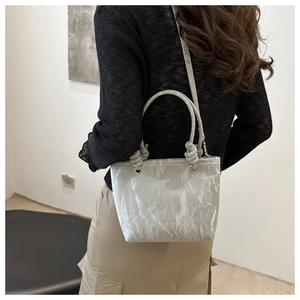 Detail view of silver pleated handbag with knot handles worn by a model in a minimalist setting