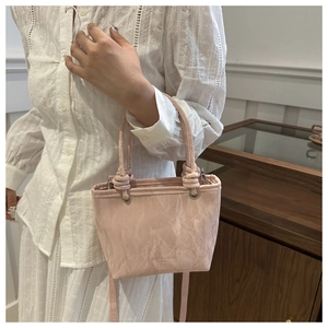 Close-up of pink bucket bag with knotted handles and fashion logo on pleated texture