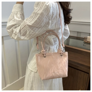 Detail of light pink textured leather handbag with dual tubular handles and slim shoulder strap