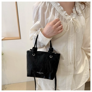 Detail of black pleated tote bag featuring knotted handles and white printed lettering