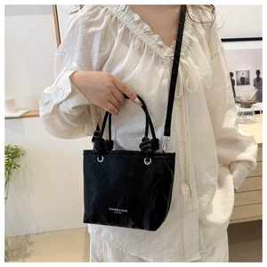 Detail of black pleated faux leather bucket bag with knotted handle and silver metal eyelets