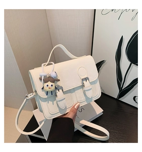 Detail view of white vintage mini bag with flap buckles, top handle, and cute doll pendant