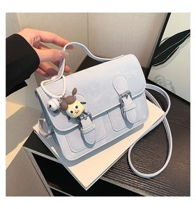 Detail view of a light blue square handbag featuring twin buckle straps and a cartoon charm