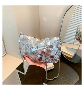 Detailed view of large silver sequins on a luxury chain bag held by hand in soft light