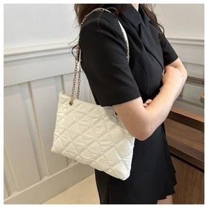 White quilted tote bag with gold chain straps shown on a model against a clean wall