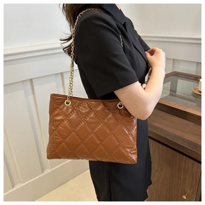 Close-up of brown quilted tote bag with gold chain strap on model in a cozy room