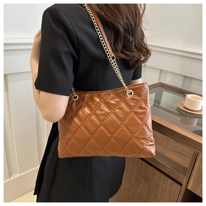 Close-up of brown quilted tote bag with gold chain strap worn by a model in a cozy room