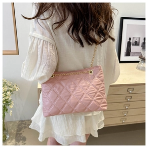 Pink quilted tote bag with golden chain straps shown on person in cozy indoor setting