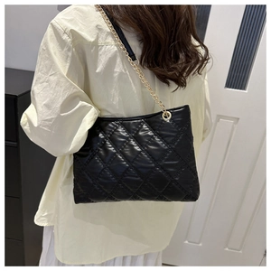 Close-up of black quilted tote bag with gold chain strap worn by a female model