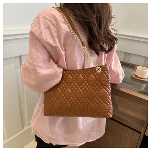 Detail of brown quilted leather bag with gold chain strap on a model shoulder