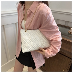 Detail view of the white quilted crossbody bag with gold chain strap on a female model
