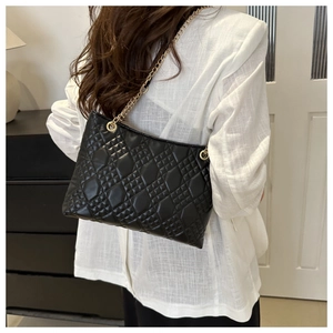 Close-up of black quilted leather shoulder bag with gold chain strap on a white shirt