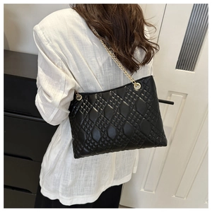 Woman wearing a large black quilted tote bag with gold chain straps in a home setting