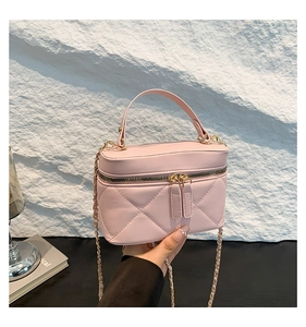Detail of pink quilted box bag with dual zippers and gold chain strap held by hand