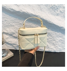 Detail of a beige quilted box bag featuring a top handle and metallic chain strap