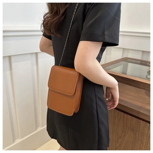 Brown rectangular leather phone bag with chain strap shown on model's shoulder