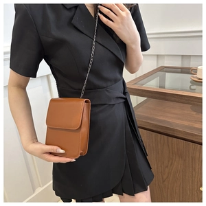 Brown leather crossbody bag with dark grey chain strap shown on black dress